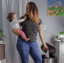 A mother holding a baby and disposing of a wipe in the trash bin