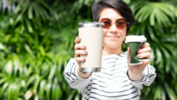 Stylish Asian woman smile, hold and show reusable stainless insulated tumbler and squeeze single use paper coffee cup with green foliage. Say no to plastic, Eco friendly and zero waste concept