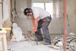 Builder digging up the house floor, lifting up old tiles with a crowbar. House renovation.