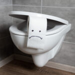 Sad emoticon on white toilet paper on toilet bowl in modern restroom